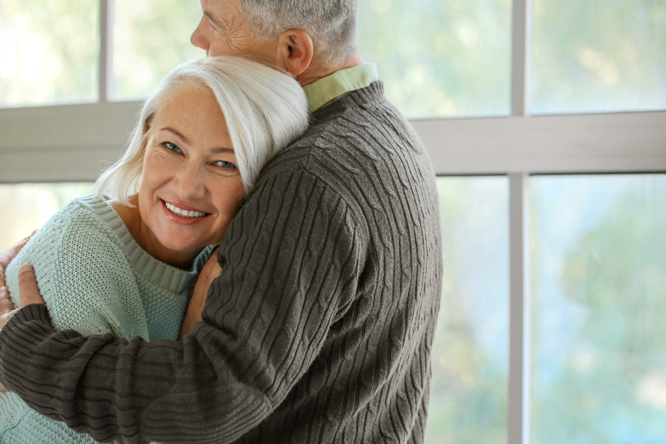 Couple de retraités enlacés près d'une fenêtre